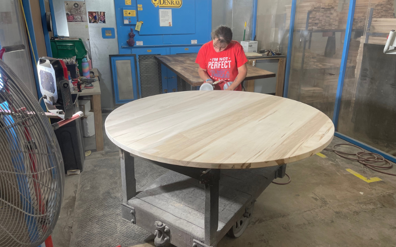 A worker at the Bassett, Va. BenchMade plant is seen sanding the edges of a solid wood dining table top.