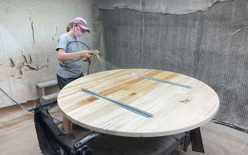 Here, an employee is seen applying a finish to a solid wood dining table top at the Bassett facility.