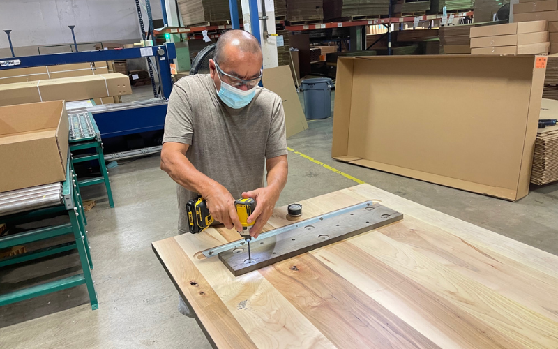 An employee at the Bassett, Va. plant affixes a solid wood plate to the bottom of a table. This plate will connect the table to the base.