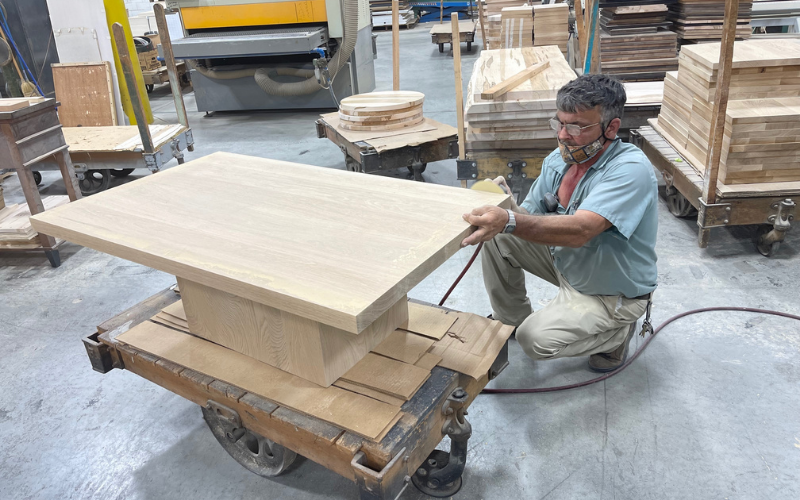 Occasional tables are among the products that flow through the Martinsville plant. A worker is seen sanding the edges of a solid wood cocktail table.